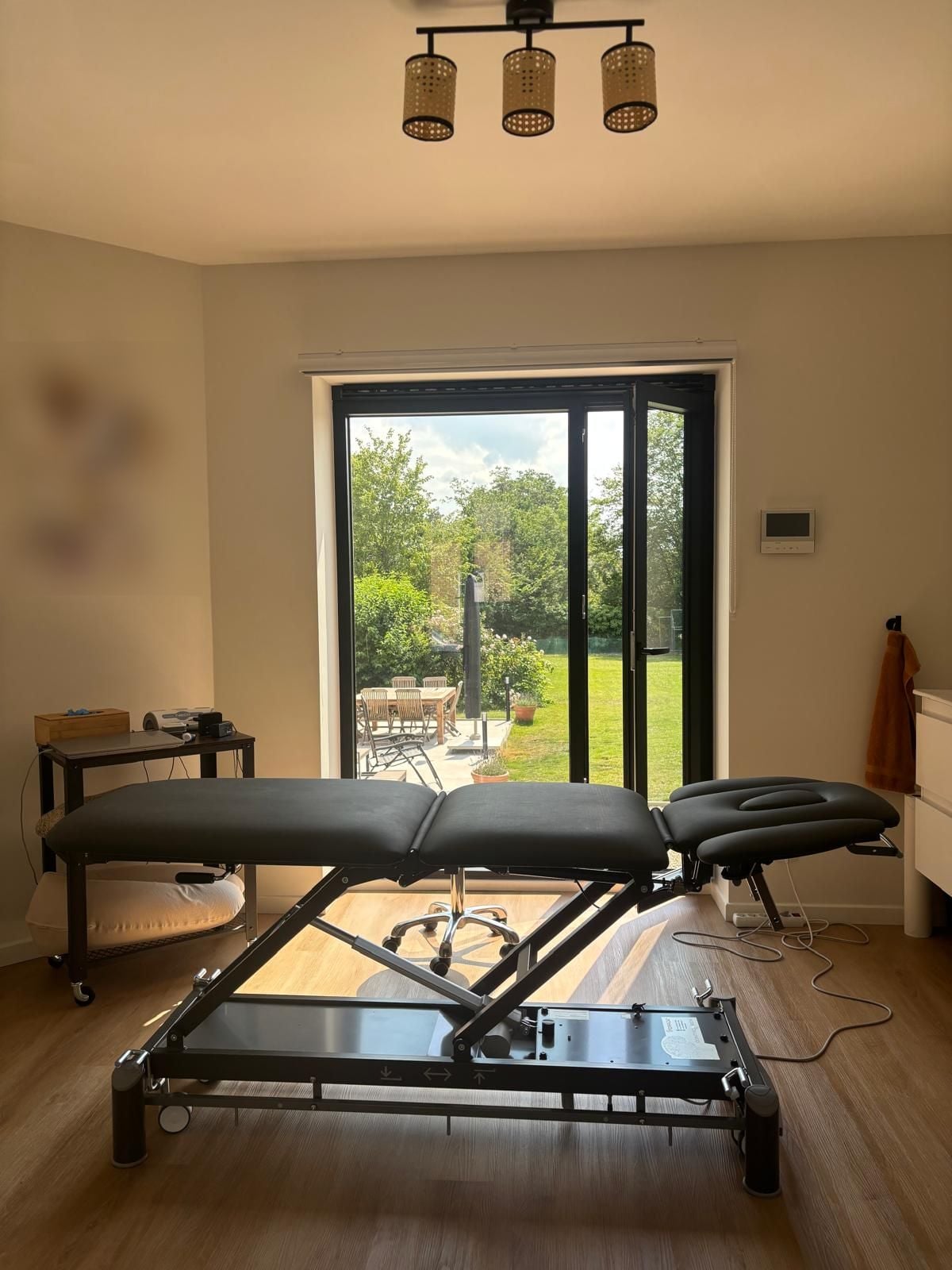 Salle de soin avec table de kinésithérapie face à la baie vitrée ouverte sur le jardin